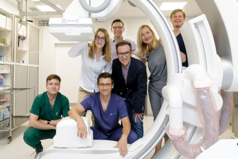 Grupa osób pozująca do zdjęcia w pomieszczeniu medycznym. Stoją obok urządzenia do rezonansu magnetycznego.