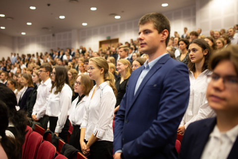 A group of young people dressed smartly stand in rows of red chairs in the auditorium.