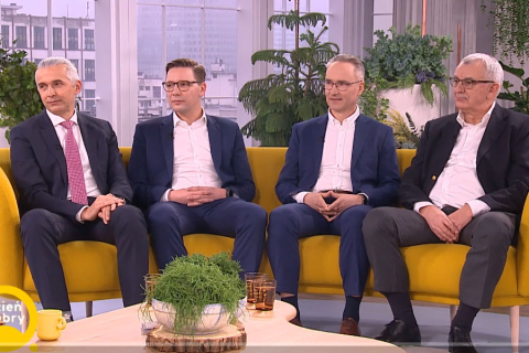 Czterech mężczyzn w garniturach siedzi na kanapie.