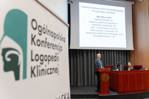 Conference room with banner ‘National Conference on Clinical Logopaedics’. On stage, a man at the lectern ‘VERITATIS SPLENDOR’. In the background, a screen with a presentation about cochlear implants at the Department of Otorhinolaryngology, WUM.