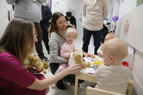 Grupa osób na szpitalnym korytarzu. Część z nich to dzieci. Wszyscy się uśmiechają.