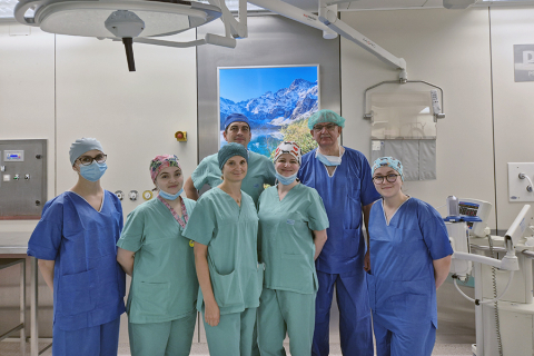 Transplant team. Seven people wearing surgical gowns stand in the operating room and pose for a photo.
