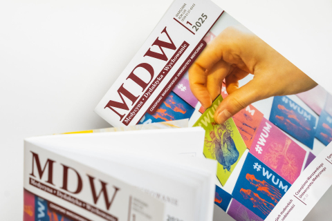 Ręka osoby unosi kolorową okładkę egzemplarza czasopisma „MDW”. Na okładce widać tytuł oraz kolorowe ilustracje z motywami medycznymi. Obok leży otwarty numer czasopisma. Kompozycja podkreśla tematykę publikacji i jej nowy numer.