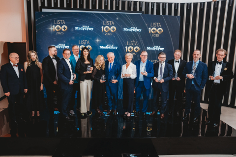 A group of people standing on stage during the ‘Puls Medycyny 2025 List 100’ gala, holding award statuettes against a backdrop featuring the event’s logo.