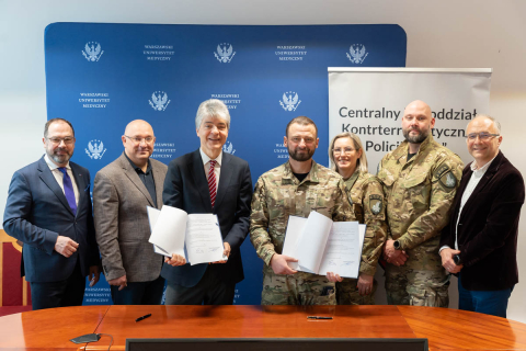 Six men and one woman pose for a photo. The two men in the center are holding open folders with a document. Behind them are two backdrops: one blue with the WUM logo and another with the logo and the inscription 'Central Counterterrorism Subunit of the Police BOA'