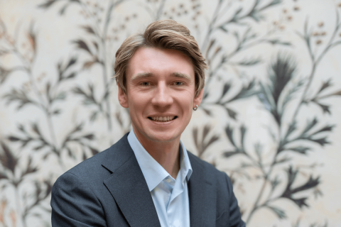 Prof. Jakub Piwowarski, młody mężczyzna pozujący do zdjęcia w ciemnej marynarce i jasnej koszuli.