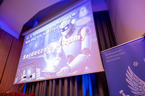 A conference room with a large screen displaying a graphic of a robot and the text: ‘AI in Higher Education: Don’t Get Left Behind. A Warm Welcome’. Next to it stands a blue banner of the Medical University of Warsaw.