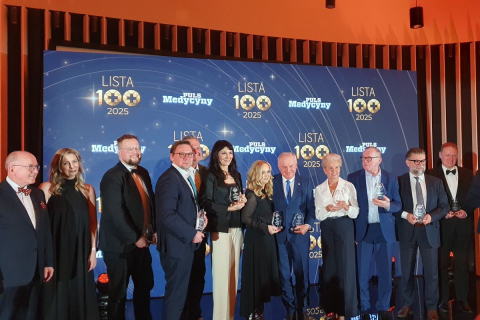 Grupa osób stojących na scenie podczas uroczystej gali „Lista 100 Pulsu Medycyny 2025”, trzymających statuetki wyróżnienia na tle ściany z logo wydarzenia.