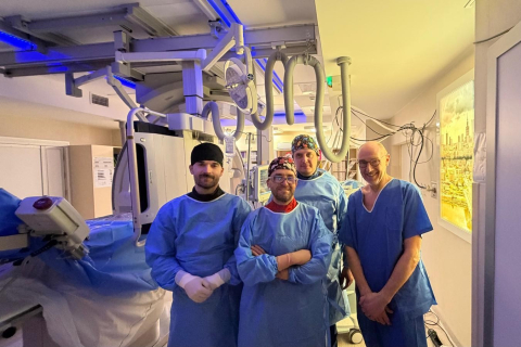 A team of medical staff in the treatment room, dressed in sterile gowns and gloves, standing next to specialized medical equipment.