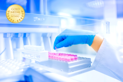 Laboratorium medyczne. Na planie główny ręka osoby w białym fartuchu. Na dłoni niebieska rękawiczka. Dłoń umieszcza małe fiolki z różowymi zakrętkami w specjalnym pojemniku.