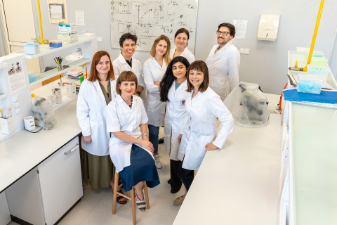 Osiem osób ubranych w białe fartuchy pozuje do wspólnego zdjęcia w przestrzeni laboratoryjnej.