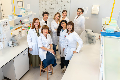 Zespół naukowców ubranych w białe fartuchy medyczne, pozują do wspólnego zdjęcia w pomieszczeniu laboratoryjnym.