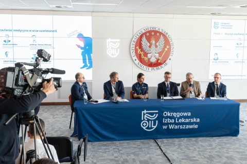 Sześcioro uczestników bierze udział w panelu dyskusyjnym. Przed stołem panelowym ustawiona jest kamera rejestrująca wydarzenie.
