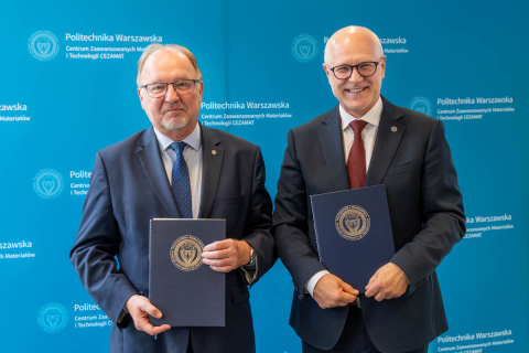 Dwie osoby stoją przed ścianką z logo Politechniki Warszawskiej i Centrum Zaawansowanych Materiałów i Technologii CEZAMAT. Każda z osób trzyma dokument z godłem uczelni.