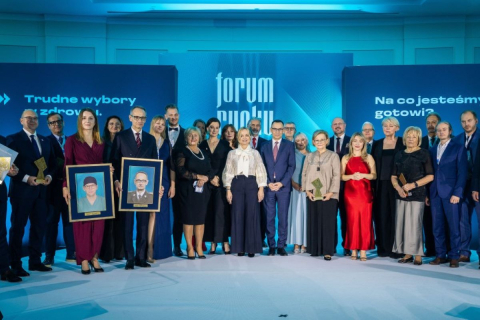 Grupowe zdjęcie uczestników wydarzenia „Forum Rynku Zdrowia” na scenie. Dwie osoby trzymają oprawione portrety, a część uczestników prezentuje statuetki.