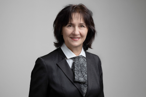 Portret osoby w ciemnym garniturze, białej koszuli i wzorzystym krawacie, na jasnoszarym tle